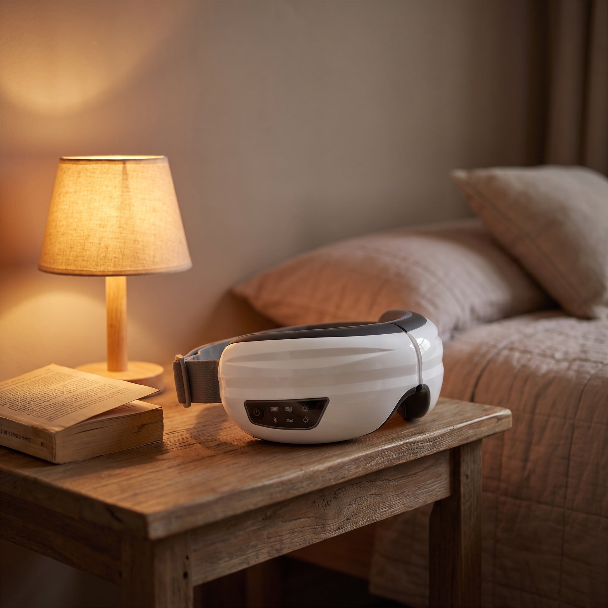 The Velto Heated Eye Massager resting on a bedside table in warm evening light